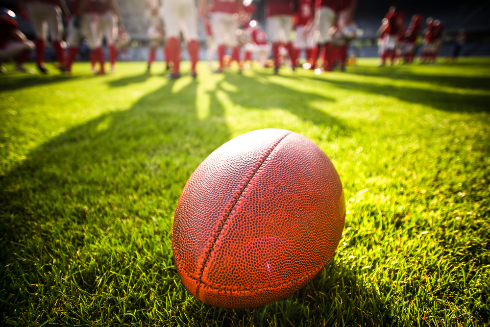 close up of an american football on the field, players in the background