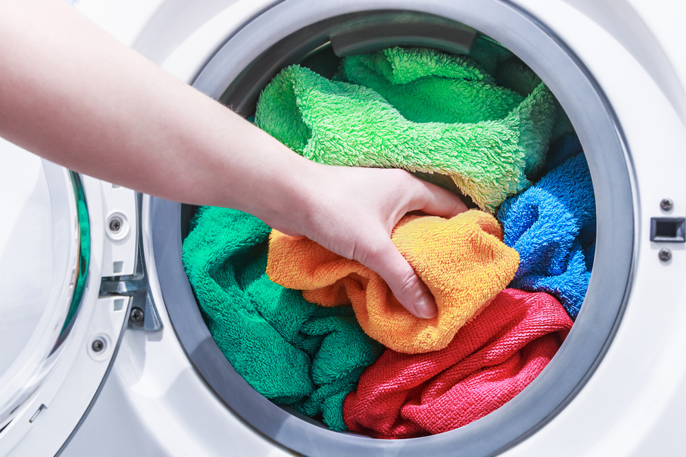 hand and puts the laundry into the washing machine. focus on a colored towel