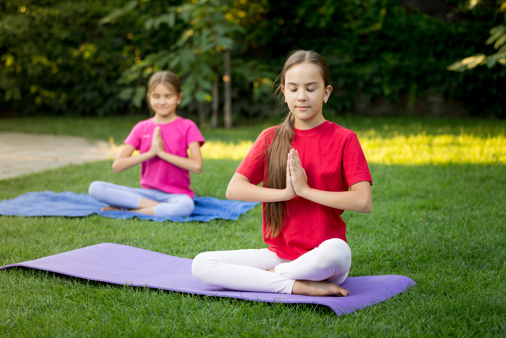 Two smiling sisters practicing yoga on grass at sunny park